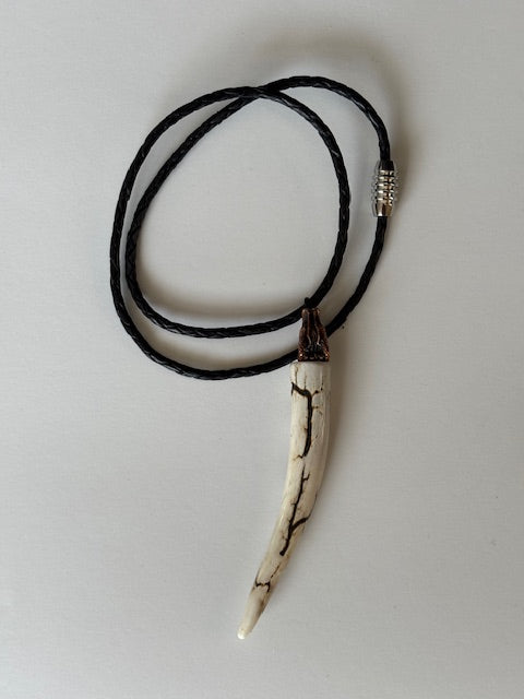 Deer antler tips necklace polished and with black strike attached to a metal wolf head with a black leather cord on a gray background