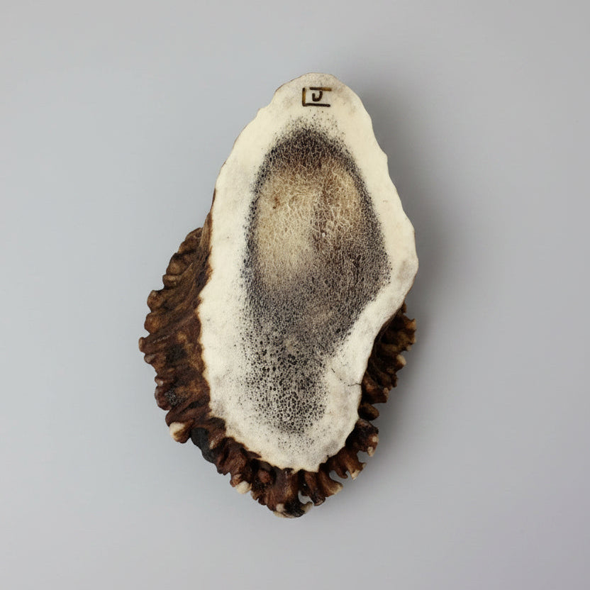 bottom view with the signature of the artist of the Decorative elk antler cornet with a spirit turtle engraved and inlayed on a gray background