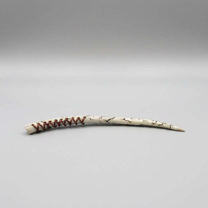 Long, thin wand made of a long antler tip with decorative leather patterns on a gray background