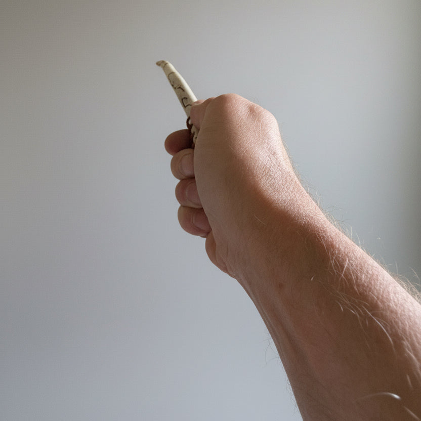 hand holding a long, thin wand made of a long antler tip with decorative leather patterns on a gray background