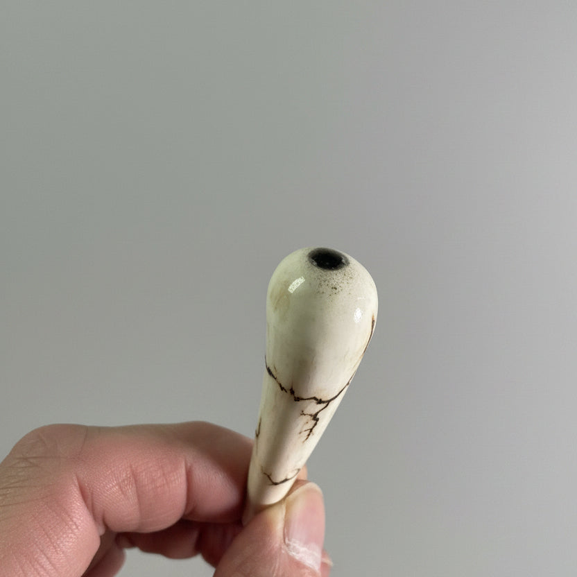 A hand holding a dragon tooth like made of a deer antler tip with black strike on a gray background