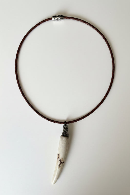 Deer antler tips necklace polished and with black strike attached to a metal wolf head with a black leather cord on a gray background