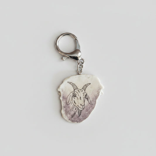 Silver keychain with goat engraved on piece of deer antler on a gray background