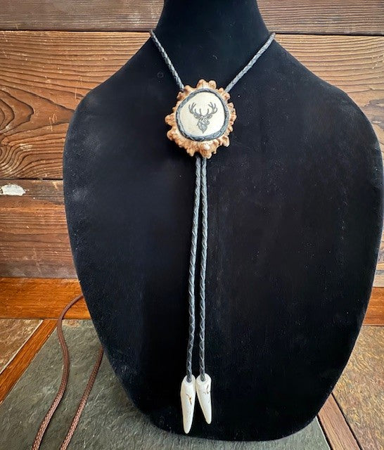 Bolo tie with deer emblem on a black mannequin bust against a wooden background