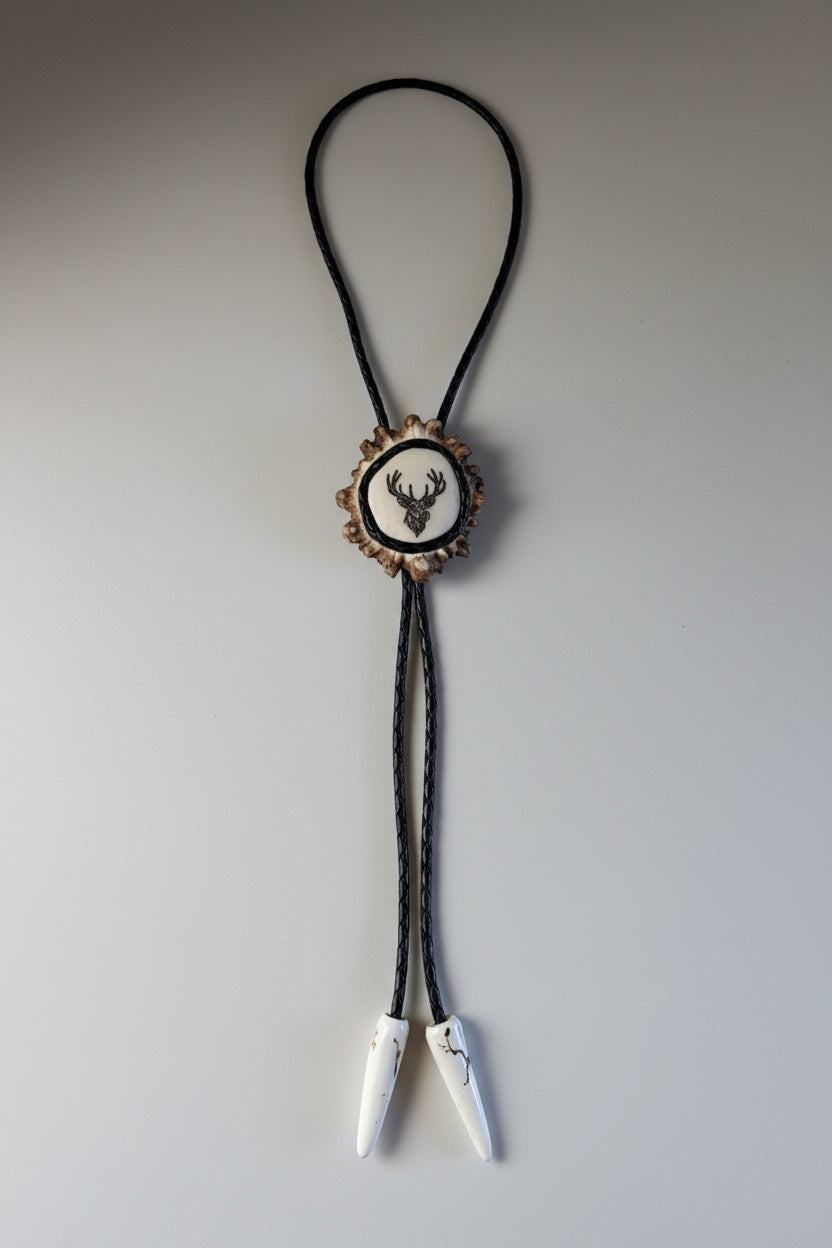 engraved elk bolo tie on a moose antler cornet on a gray background